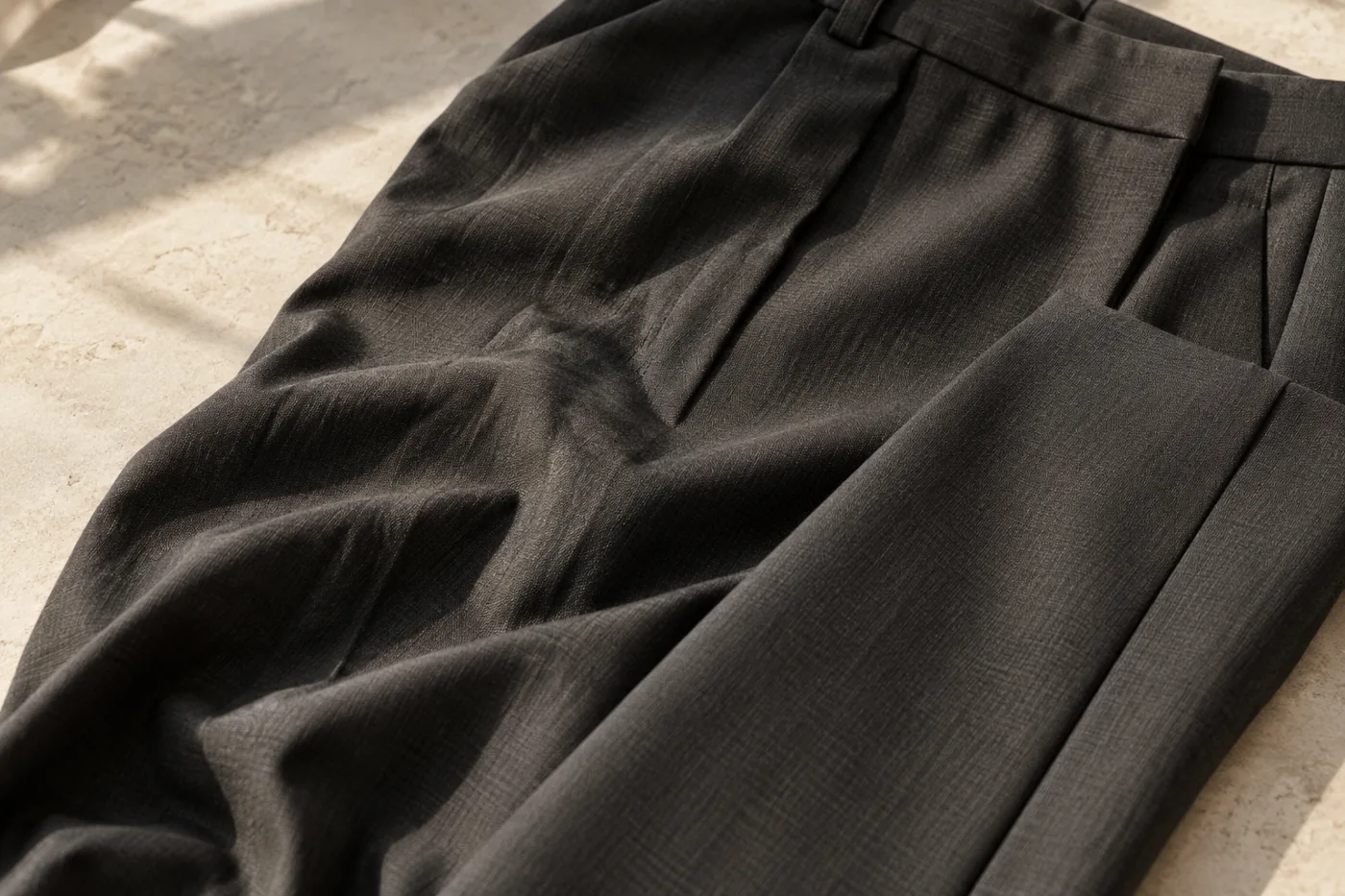 Charcoal tailored trousers laid flat with visible creases across the fabric.
